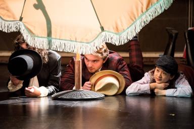 Fabian, Sir Toby, and Sir Andrew hide behind a fringed umbrella